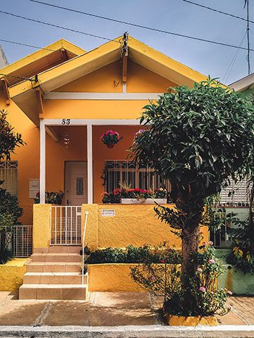 An image of one story yellow house with a small tree outside it